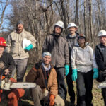 Seven Appalachain Trail volunteers wearing PPE and holding chainsaws gather for a group photo.