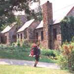 Hiker carrying pack stands outside stone lodge hostel
