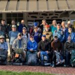 Group of twenty hikers pose with hiking gear and hangtags outside ATC headquarters in Harpers Ferry, WV.