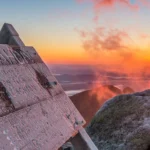 Katahdin Summit Sign with misty sunrise in the background.