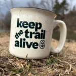 Cream colored camp mug designed with the slogan "Keep the Trail Alive".
